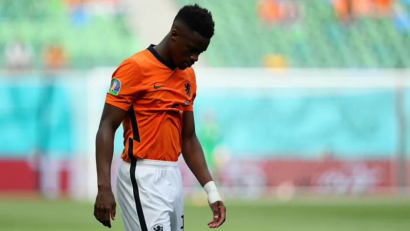 Cody Gakpo in a Netherlands jersey, looking somber, with a blurred background of a football pitch. — latest news and analysis.