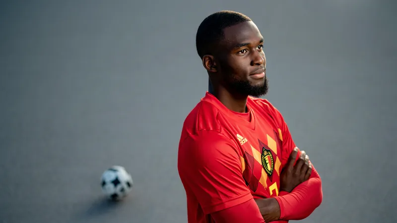Doku criticized for plan to leave World Cup for child's birth Jeremy Doku in Belgium jersey, looking thoughtful, with a football in the background.