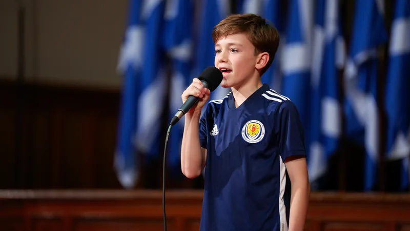 A young boy in a Scotland football shirt singing into a microphone
