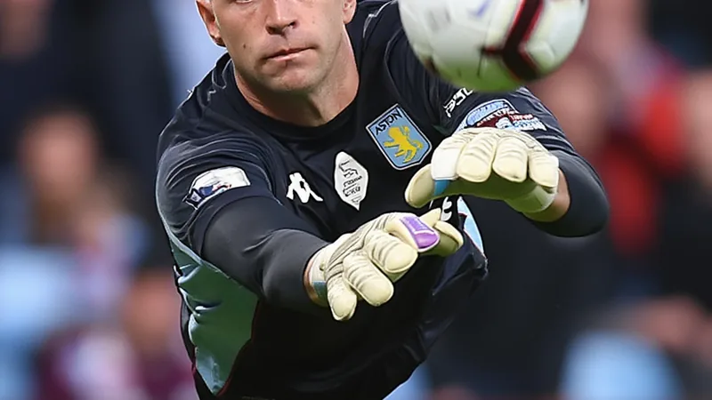 Juventus Target Emiliano Martínez After Alisson Deal Collapses Emiliano Martínez in Aston Villa goalkeeper kit, diving to save a ball during a match.