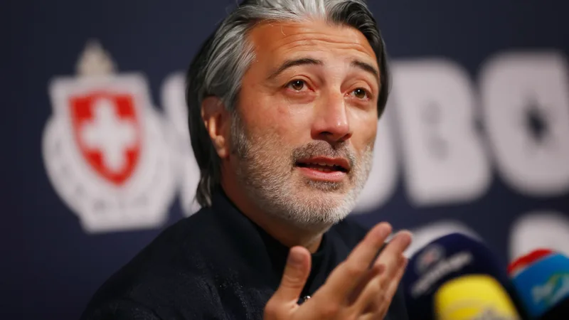 Switzerland coach Murat Yakin speaks confidently during a press conference, with the Swiss national team logo in the background.