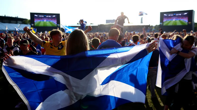 Scotland Fans Dream of Knockout Stage as Morocco Clash Looms Scotland fans celebrating in a fanzone with big screens showing the World Cup match, Saltires waving, and a festive atmosphere.