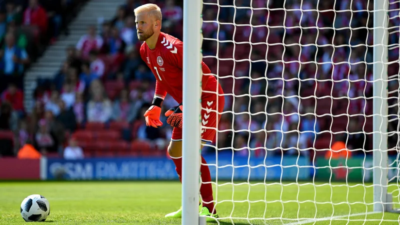 Kasper Schmeichel in goal for Denmark during a match, with a football in the foreground.