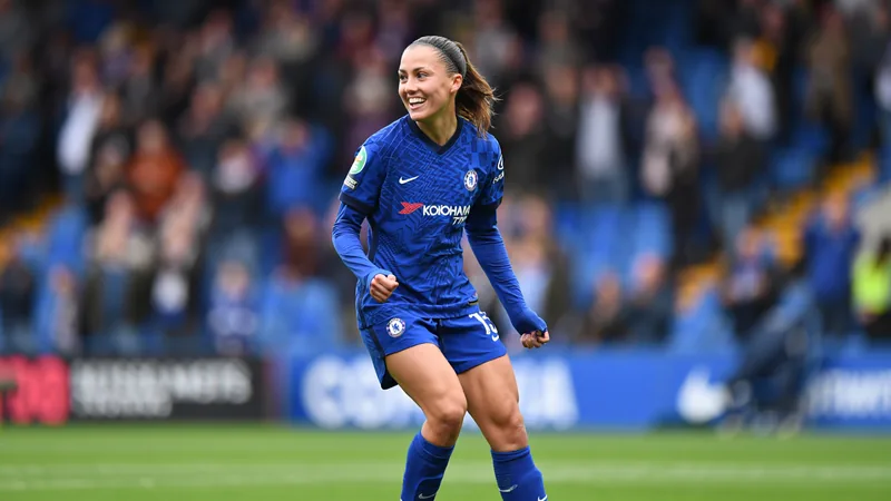 Aggie Beever-Jones in Chelsea kit, smiling during a match, with stadium background.