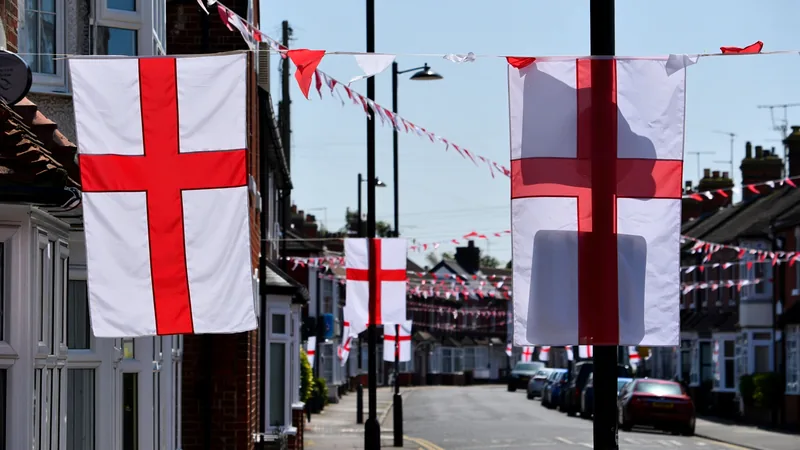 A street in Grimsby lined with St George's Cross flags hanging from lampposts and houses, with red and white bunting overhead.