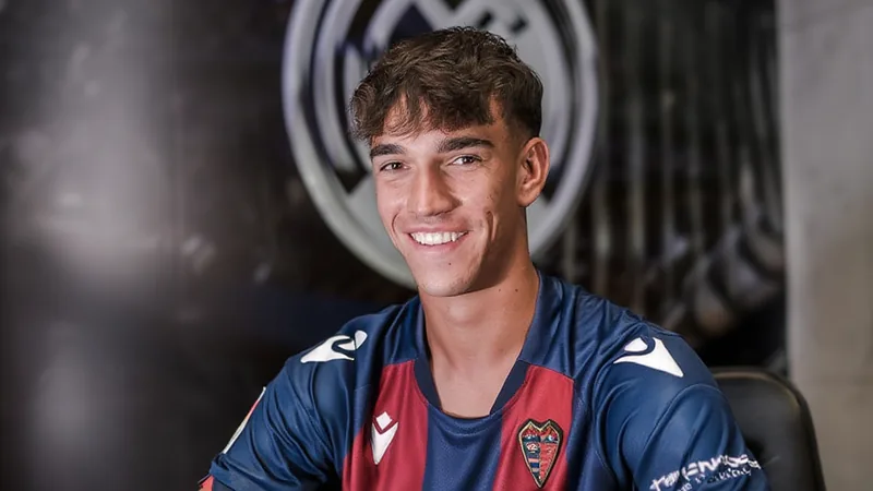 Carlos Espí in a Levante kit, with Real Madrid crest in background, signing a contract.