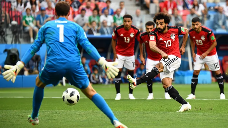 Mohamed Salah taking a penalty kick during a World Cup match, with teammates watching.