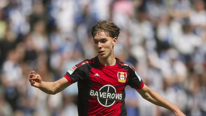 Ein junger Fußballspieler im Trikot von Bayer Leverkusen posiert auf dem Trainingsplatz, im Hintergrund die BayArena. — latest news and analysis.