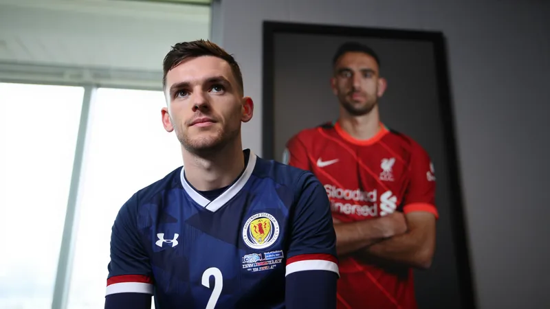 Andrew Robertson in schottischer Nationalmannschaftskleidung mit schwarzer Trauerbinde, blickt traurig, im Hintergrund ein Porträt von Diogo Jota