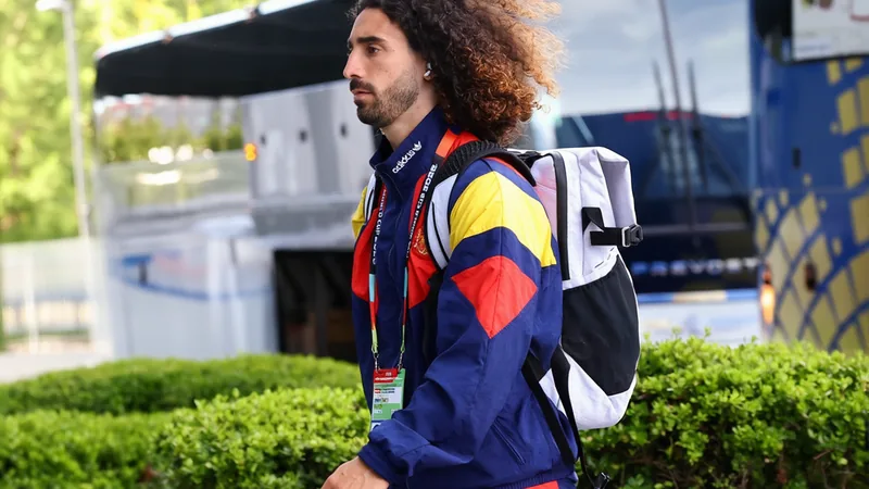 Marc Cucurella im spanischen Nationaltrikot bei seiner Ankunft im Trainingsquartier, lächelnd und winkend, im Hintergrund das spanische Teamlogo.