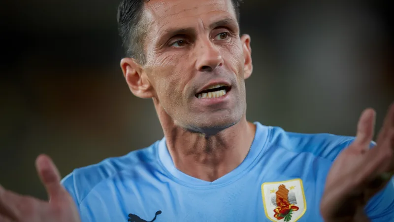Poyet über Uruguays Duell mit Spanien und Vertrauen in Darwin Núñez Gustavo Poyet in einem dunklen Anzug vor einem Mikrofon mit FIFA-Logo im Hintergrund, während er konzentriert in die Kamera spricht.