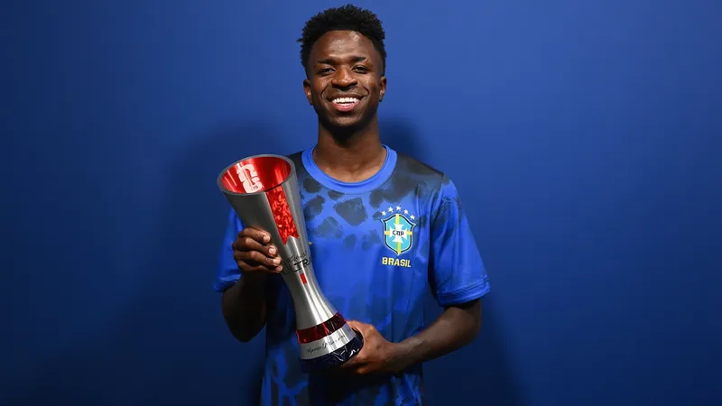 Vinícius Júnior im brasilianischen Trikot jubelt nach einem Tor, im Hintergrund die brasilianische Flagge und jubelnde Fans im Stadion.