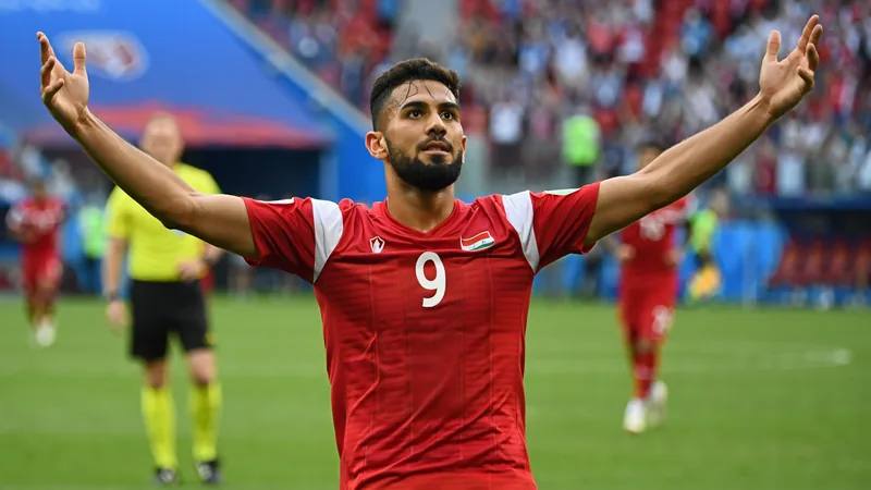 Irakischer Stürmer Aymen Hussein jubelt nach seinem Kopfballtor gegen Norwegen im WM-Spiel, im Hintergrund die irakischen Fans.
