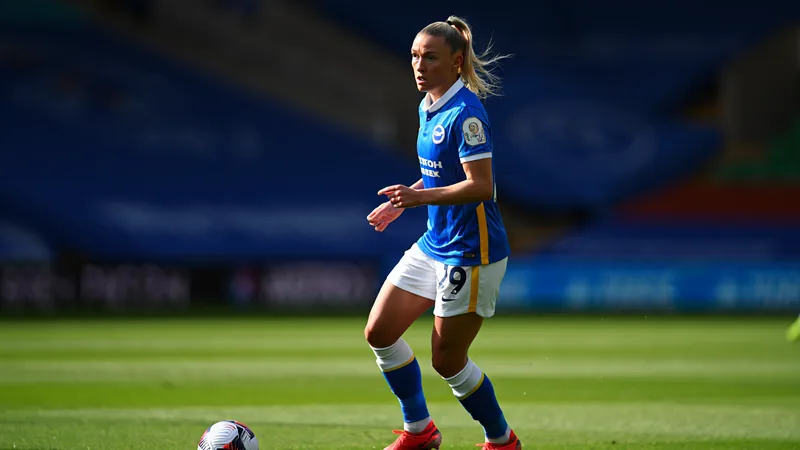 Brighton-Kapitänin Maisie Symonds im Heimtrikot mit Kapitänsbinde auf dem Spielfeld, im Hintergrund das Stadion und jubelnde Fans