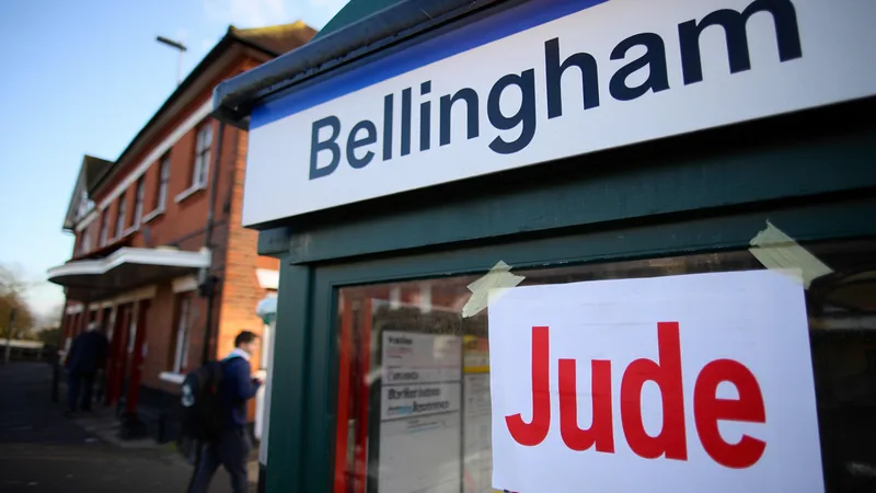 Jude Bellingham Station behält Namen bis Montag — Football World Cup Ein Bahnhofsschild mit der Aufschrift 'Jude Bellingham Station' in London, umgeben von Fußballfans, die Fahnen schwenken.