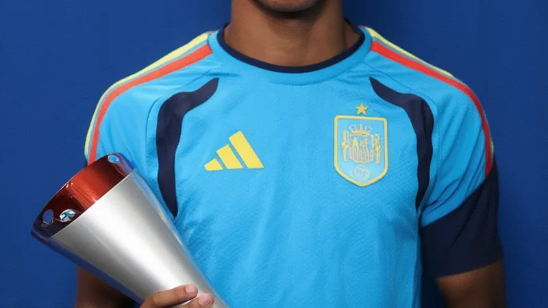 Lamine Yamal als bester Spieler des Spiels ausgezeichnet — Football Lamine Yamal im spanischen Trikot jubelt nach dem Spiel, im Hintergrund die FIFA-Weltmeisterschaftstrophäe und jubelnde Fans im Stadion.