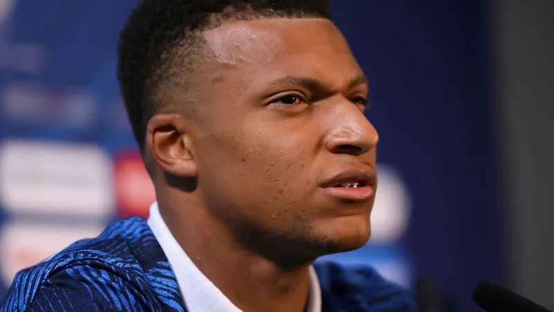 Kylian Mbappé im französischen Trikot, der nach einem Foul auf dem Rasen sitzt, im Hintergrund paraguayische Spieler und der Schiedsrichter.