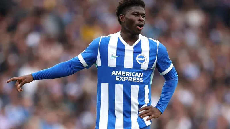 Baleba droht Saisonstart zu verpassen — Football World Cup News Carlos Baleba im Trikot von Brighton & Hove Albion, der am Knöchel verletzt am Spielfeldrand sitzt und das Spiel von der Bank aus verfolgt.