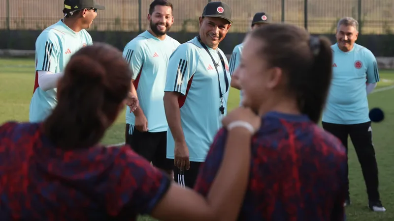 Kolumbien U-20: Paniagua vor WM 2026 — Football World Cup News Carlos Paniagua, Trainer der kolumbianischen U-20-Frauen, steht lächelnd am Spielfeldrand, im Hintergrund das Stadion von Polen.