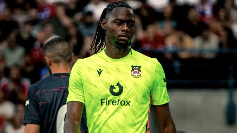 Arthur Okonkwo im Torwarttrikot von Wrexham, der den Ball fängt, während Fans im Hintergrund jubeln. — latest news and analysis.
