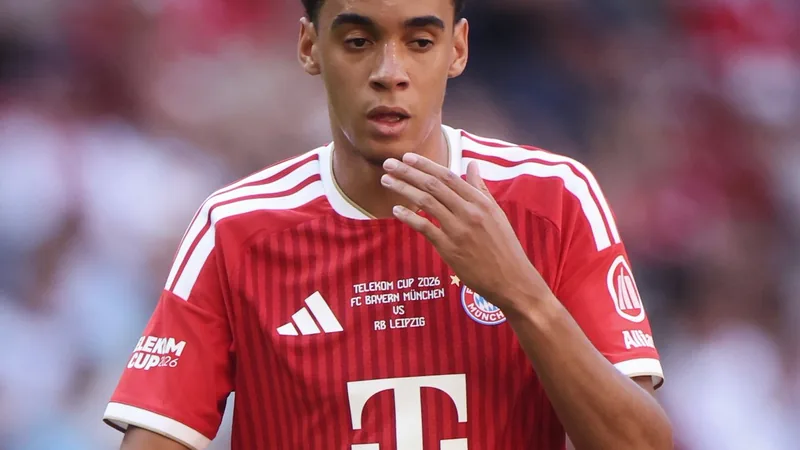 Jamal Musiala: „Mir geht es gut“ – Update zu seiner Gesundheit Jamal Musiala im Trikot des FC Bayern München lächelt während eines Interviews auf dem Trainingsplatz, im Hintergrund das Stadion.