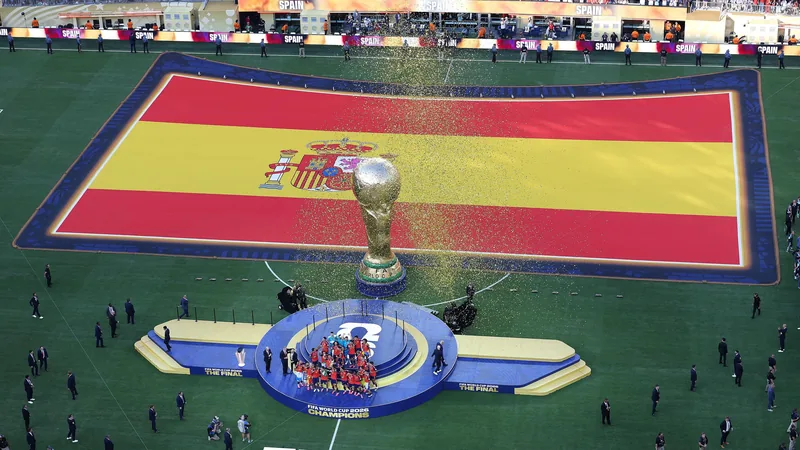 Spanische Nationalmannschaft feiert mit dem WM-Pokal im New York New Jersey Stadium, Konfetti regnet herab, Spieler in roten Trikots jubeln.
