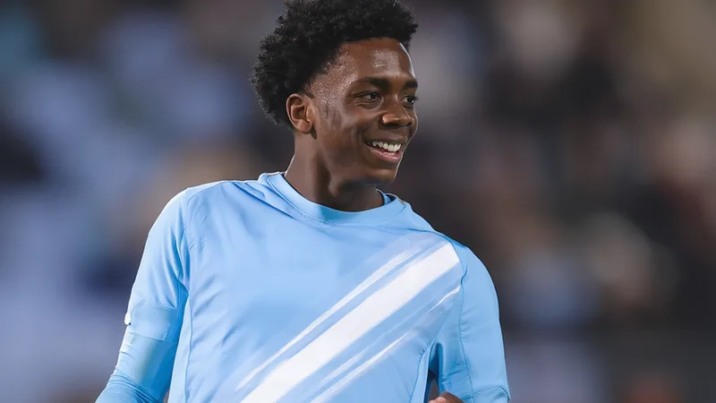 Junger Fußballspieler im Manchester-City-Trikot dribbelt auf dem Trainingsplatz, im Hintergrund das Stadion Etihad Stadium in Manchester.