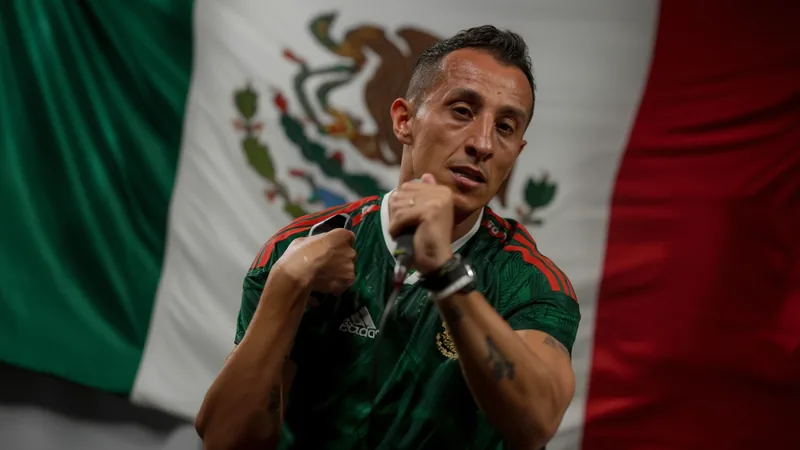 Andrés Guardado vestido con traje, micrófono en mano, comentando un partido del Mundial 2026 en un estudio de televisión con pantallas de fondo.