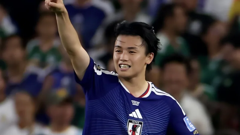 Ayase Ueda celebrando un gol con la camiseta de Japón durante el Mundial de Catar 2022, con el estadio de fondo y aficionados japoneses animando.