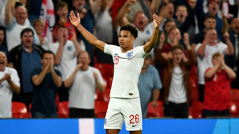 Jude Bellingham celebrando un gol con la camiseta de Inglaterra en un estadio lleno, con el marcador de fondo mostrando el resultado del partido.