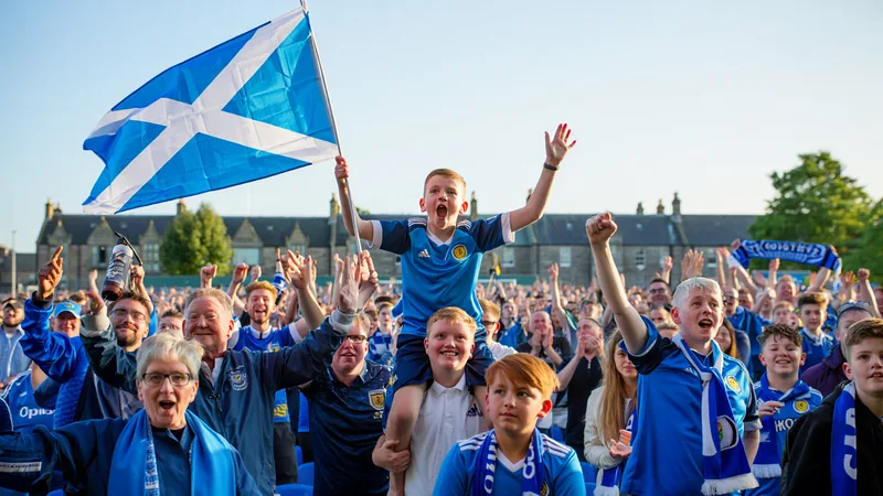 Cómo ver a Escocia en el Mundial: consejos para aficionados Aficionados escoceses con banderas y bufandas viendo un partido de fútbol en un pub abarrotado, con pantallas gigantes y ambiente festivo.