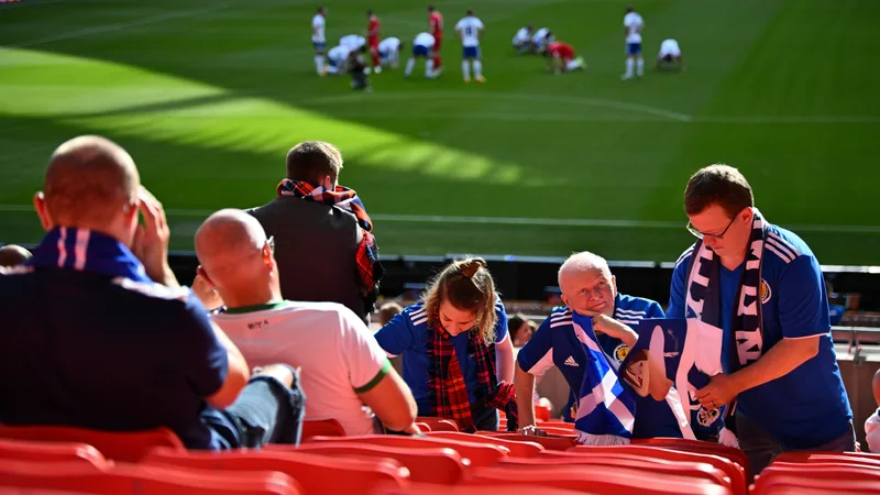 Jugadores de la selección de Escocia cabizbajos en el campo tras la derrota, con la afición escocesa al fondo animando con banderas y bufandas.