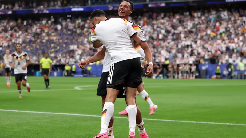 Jamal Musiala celebrando un gol con la camiseta de Alemania, haciendo el gesto de '10' con los dedos, en un estadio lleno de aficionados.