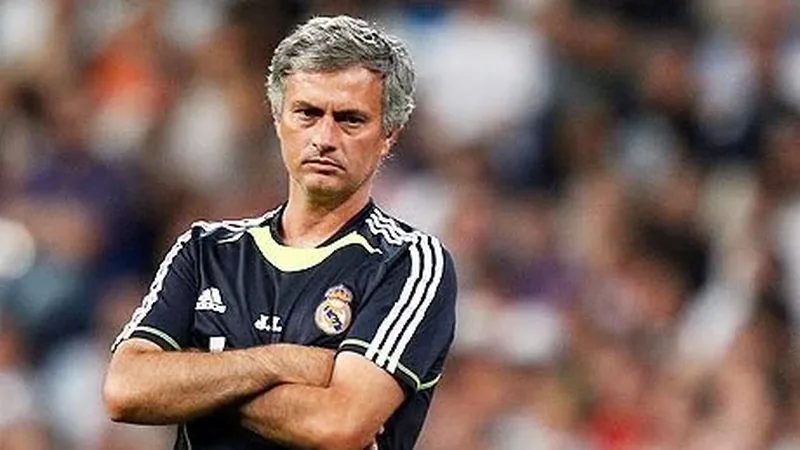José Mourinho con gesto serio, vistiendo traje oscuro, de pie en el banquillo del Santiago Bernabéu con el estadio de fondo lleno de aficionados.