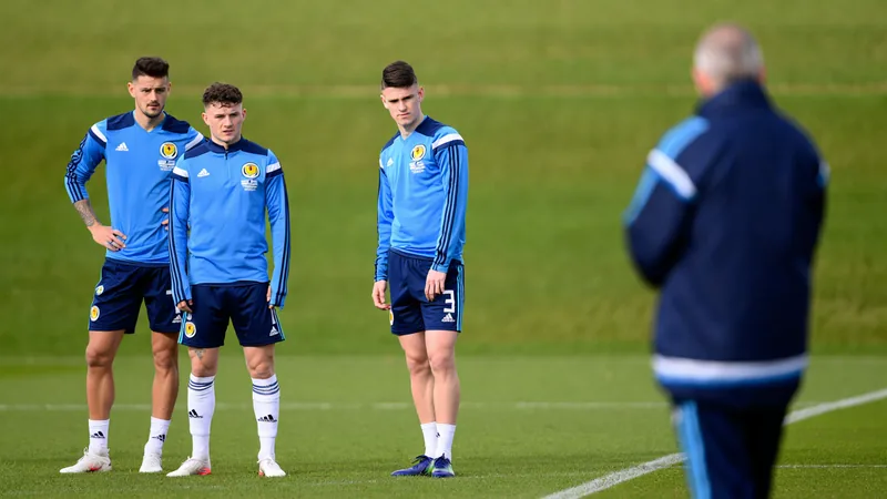 Los siete supervivientes de la primera convocatoria de Clarke con Steve Clarke, seleccionador de Escocia, dirigiendo un entrenamiento con jugadores en el campo, con la bandera escocesa al fondo.