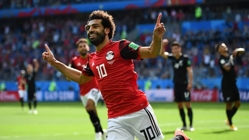 Salah anota y pone a Egipto al frente — Football World Cup News Mohamed Salah celebrando un gol con la camiseta de Egipto en un estadio lleno de aficionados, con el marcador de fondo mostrando el 2-1.