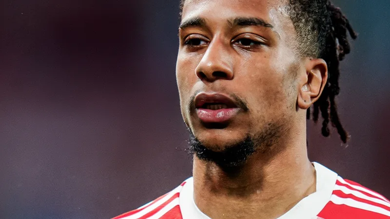 Bayern frena salida de Olise: no hay negociaciones con Real Madrid Michael Olise con la camiseta roja del Bayern Múnich celebrando un gol en el Allianz Arena, con aficionados de fondo y el marcador iluminado