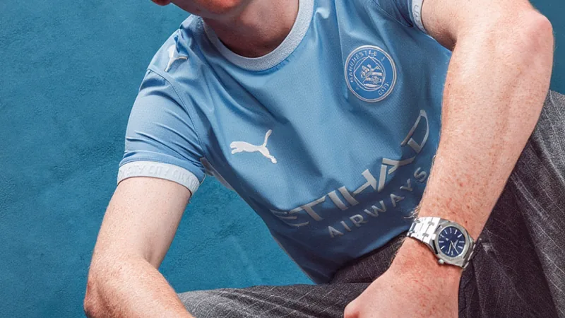 Elliot Anderson con la camiseta del Manchester City posando en el estadio Etihad, con el escudo del club y la equipación celeste.