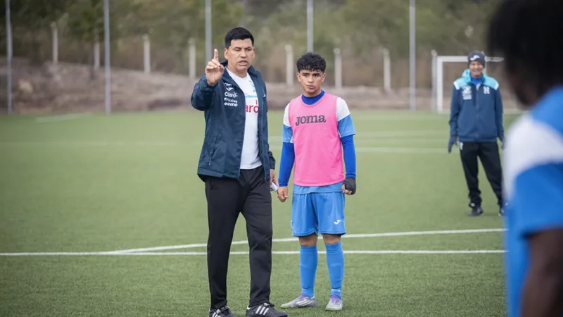 Jugadores de la selección sub-20 de Honduras celebrando un gol en un partido de fútbol, con el entrenador Orlando López al fondo.