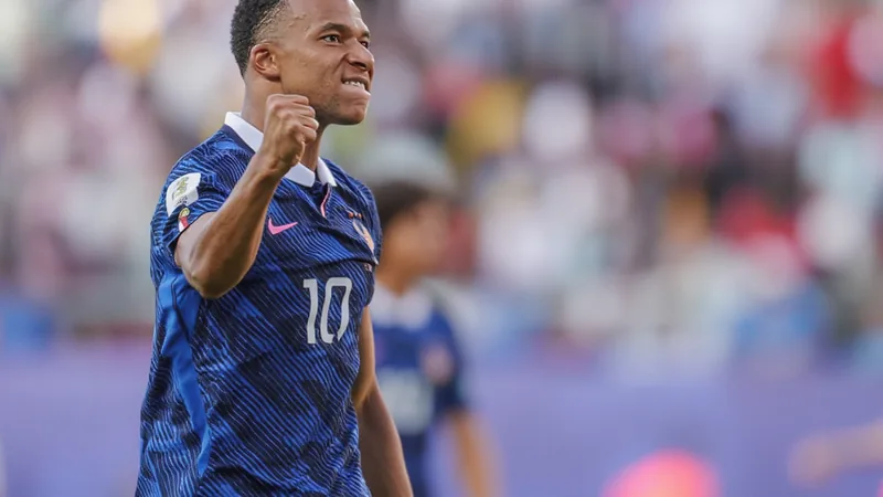 Kylian Mbappé con el uniforme de su equipo, mirando fijamente a la cámara, en un campo de fútbol durante un partido nocturno.