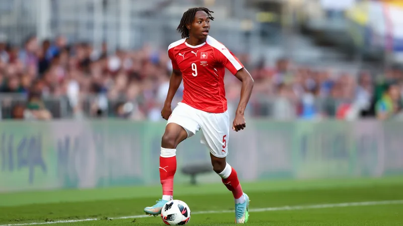 Newcastle prepara oferta por Johan Manzambi — Football World Cup News Johan Manzambi, joven futbolista suizo, con la camiseta de su selección en un partido del Mundial sub-17, celebrando un gol con el puño en alto.