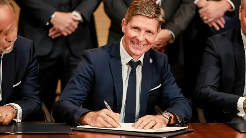Oliver Glasner firma por tres años con el Nottingham Forest Oliver Glasner sonriendo con una bufanda del Nottingham Forest en el estadio City Ground, con el césped y la grada de fondo.