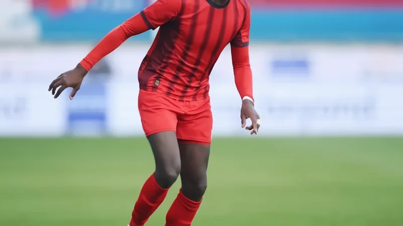 Omar Touré posa con la camiseta del Watford en el estadio Vicarage Road, con el césped de fondo y el escudo del club visible.