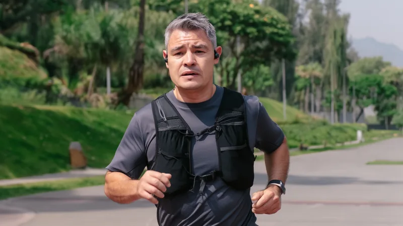 Un corredor en ropa deportiva corriendo por una calle de la Ciudad de México con edificios y montañas de fondo, bajo un cielo despejado.