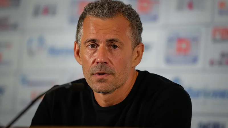 Luis Enrique, entrenador del PSG, con los brazos cruzados en el banquillo durante un partido de la Champions League, con el estadio lleno de fondo.