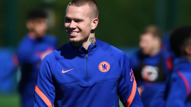 Mykhaylo Mudryk con la camiseta del Chelsea entrenando en el campo de Stamford Bridge, con el estadio de fondo y aficionados animando.