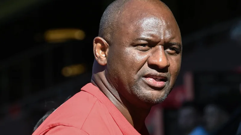 Patrick Vieira, nuevo seleccionador de Senegal — Football World Cup Patrick Vieira sonriendo con una bufanda de Senegal al cuello, en una rueda de prensa con el logo de la Federación Senegalesa de Fútbol de fondo.