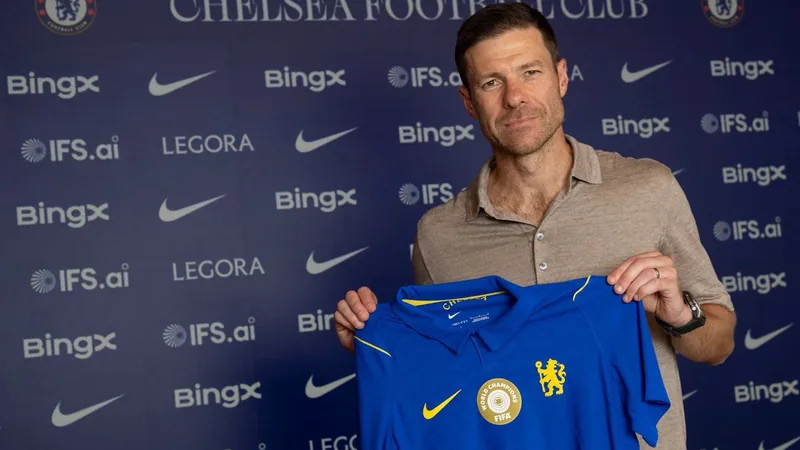 Xabi Alonso sonriendo con la bufanda del Chelsea al cuello en Stamford Bridge, con el césped del estadio de fondo y la multitud animando.