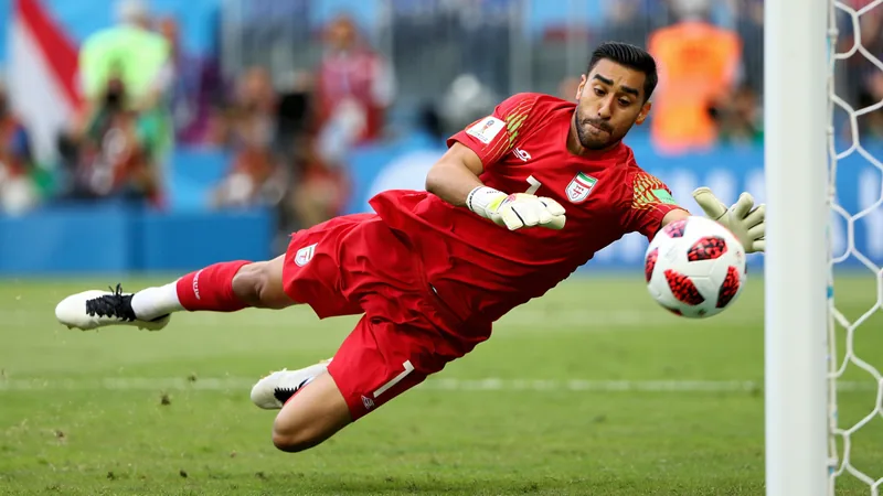 Le gardien iranien Alireza Beiranvand plonge pour arrêter un tir lors du match Belgique-Iran, sous les yeux des supporters.
