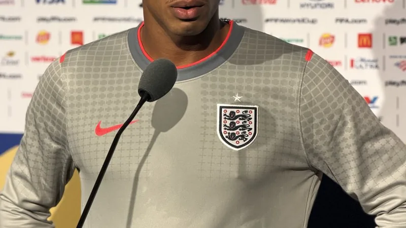 Jude Bellingham en tenue de l'équipe d'Angleterre, regardant l'horizon d'un air déterminé sur la pelouse d'un stade de football.